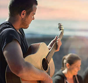 Man playing acoustic guitar for friends on beach