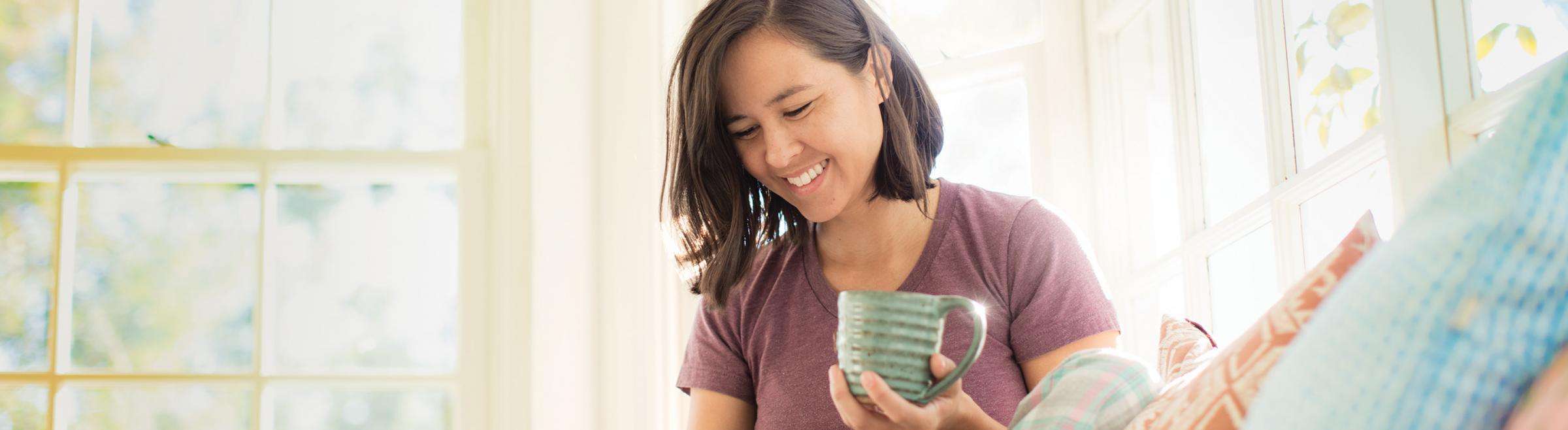 Woman drinking coffee and smiling in bright living room
